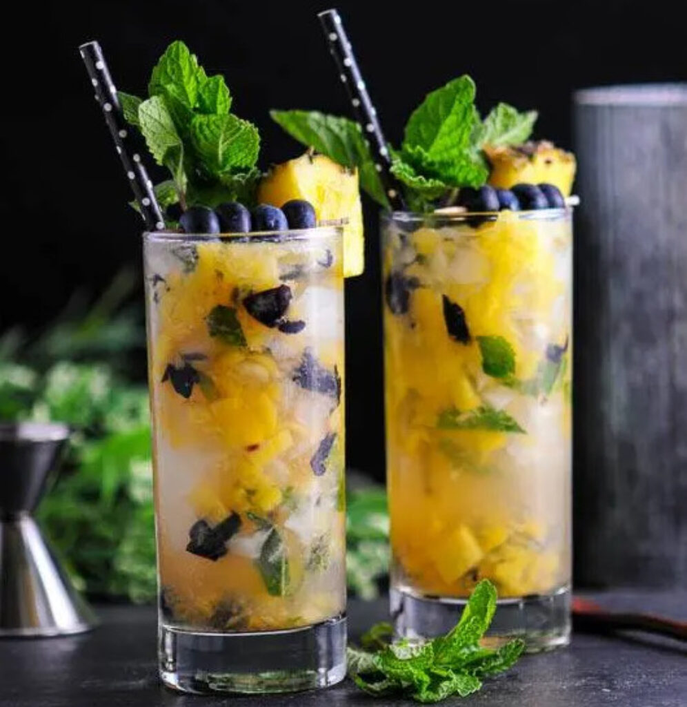 Blueberry mojito cocktail with pineapple wedge and mint