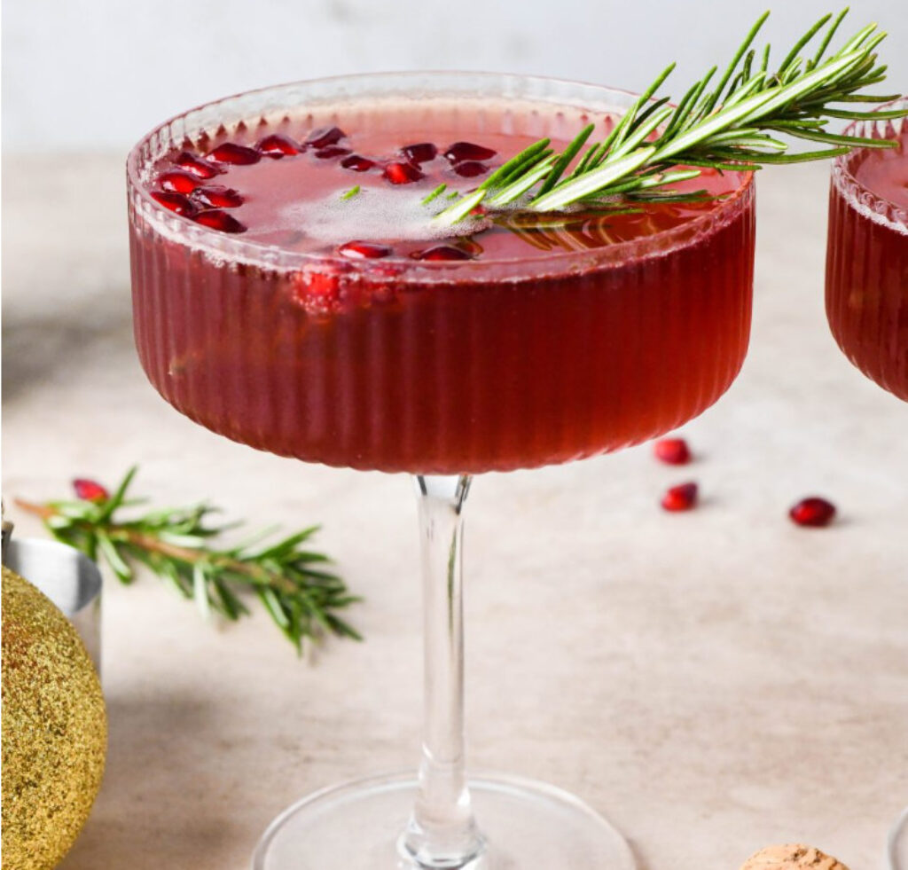Pomegranate cocktail glowing red with rosemary garnish